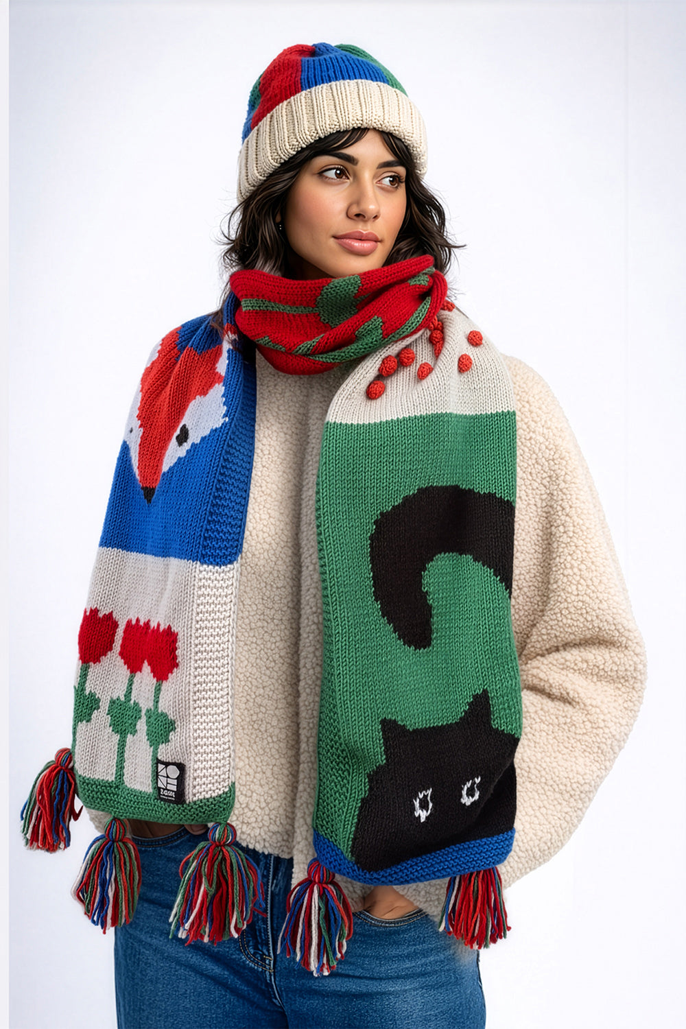 Woman wearing a colorful knitted sweater with abstract patterns on a white background. Mozaika Collective handcrafted scarf with cat and fox illustration, Berlin